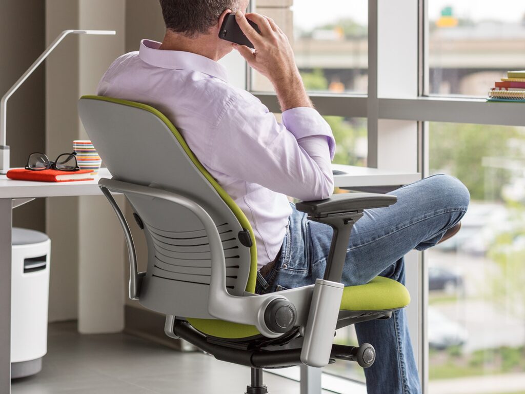 Man sitting on green and grey Steelcase Leap chair in his office.