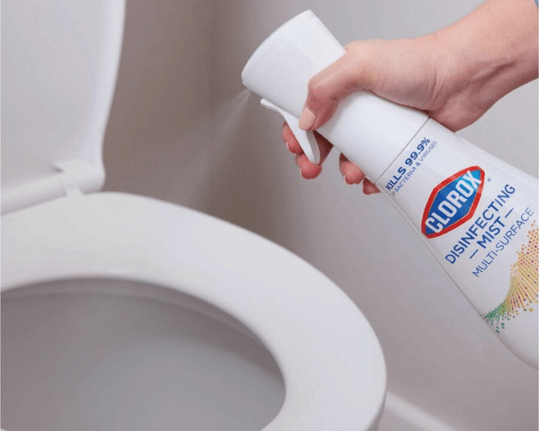 Person spraying Clorox Disinfecting Mist onto a toilet seat with a spray bottle in hand.