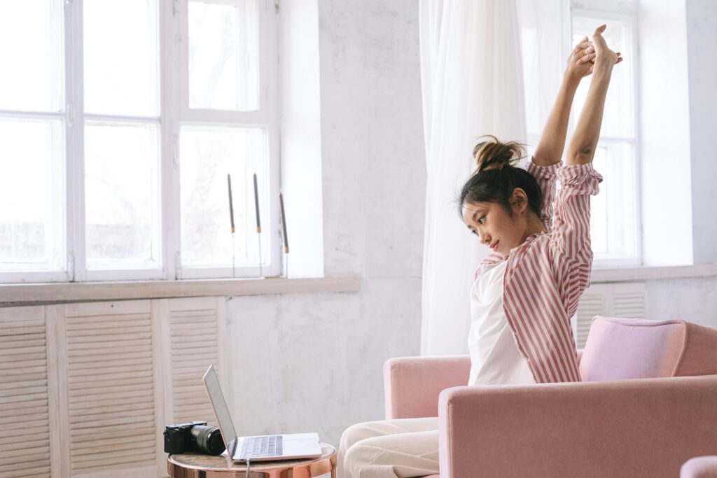 A young woman in a striped shirt stretches while working from home on her laptop. Photographer: Ivan S