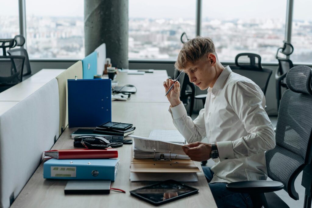 Man sitting in a chair in his office looking over some documents thoughtfully. Photographer: Mikhail Nilov.