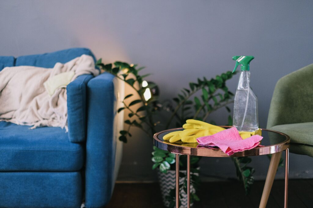 Modern living room with cleaning supplies on a table, featuring a blue sofa and indoor plants. Photographer: SHVETS production. 