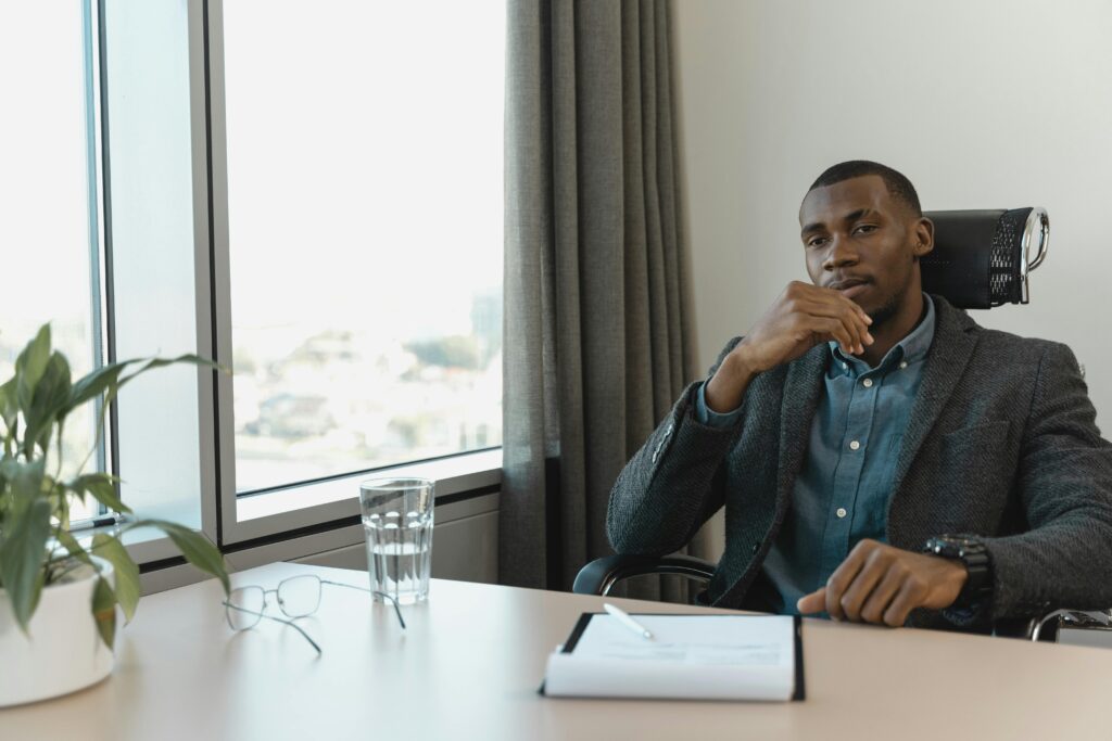 Man sitting in a chair in his office looking thoughtful. Photographer: Tima Miroshnichenko.
