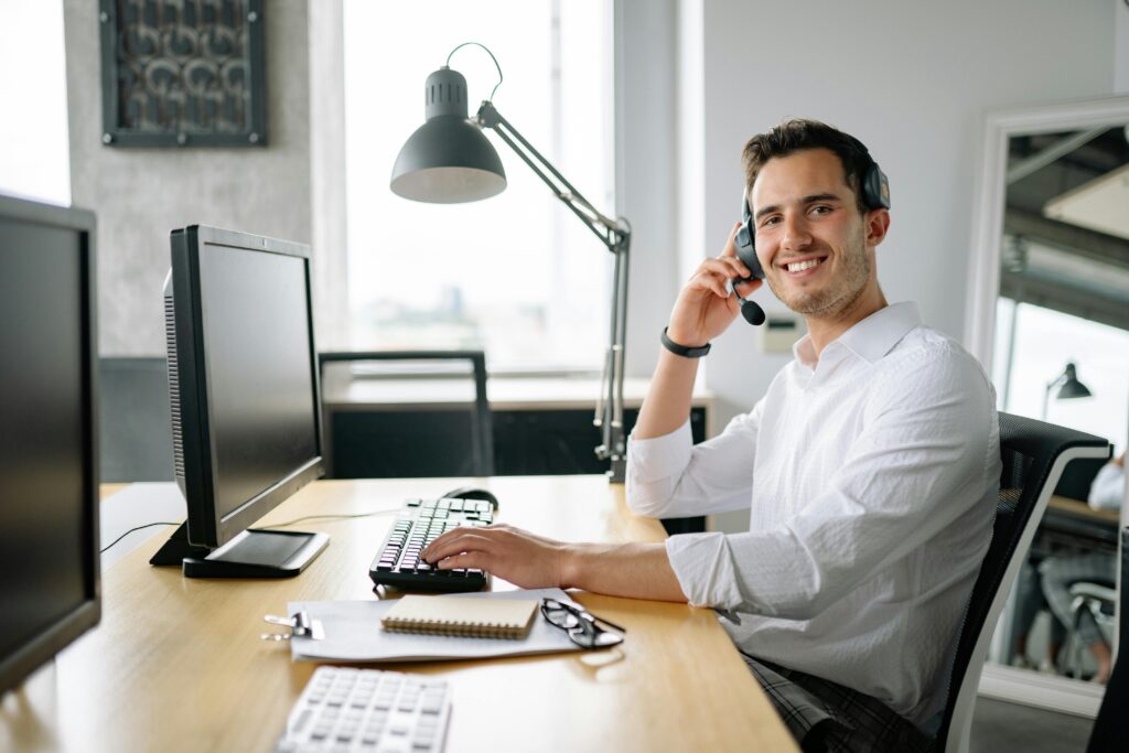Smiling call center agent working at a desk with a headset and computer in a modern office. Photographer: Yan Krukau